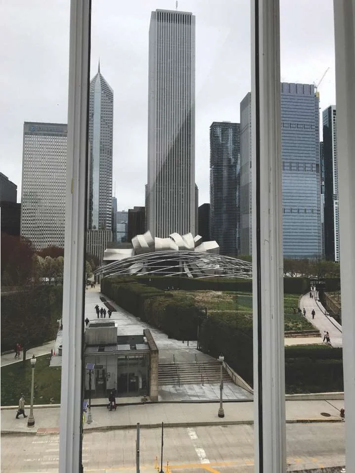 Chicago skyline above Millennium Park and the Jay Pritzker Pavilion, framed by a tall window
